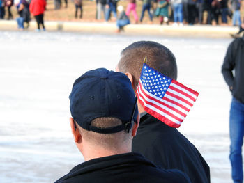 Rear view of man with small american flag in cap on street