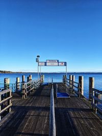 Empty pier on sea against clear blue sky