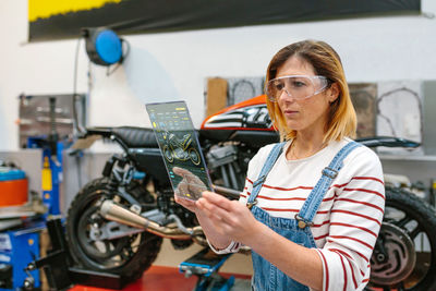 Female mechanic using transparent digital tablet with motorcycle diagnosis app