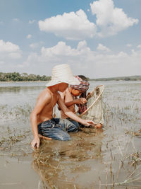 Side view of shirtless man holding water against sky