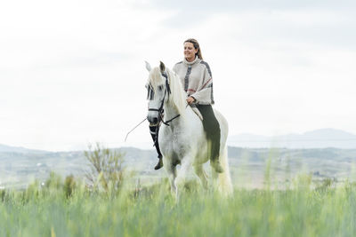 Smiling young woman riding horse at countryside