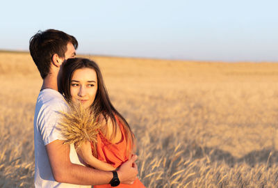 Young man hugging his girlfriend on sunset in wheat field. copy space, love, togetherness concept.