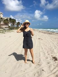 Full length of smiling young woman standing on sand at beach during sunny day