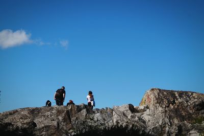 Low angle view of people on cliff against blue sky