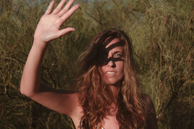 Portrait of young woman gesturing while standing against plants