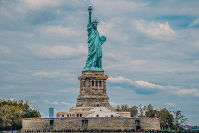 People at statue of liberty against cloudy sky