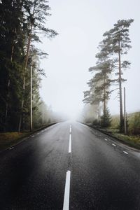 Empty road amidst trees against clear sky