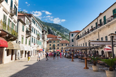 People on street amidst buildings in town against sky