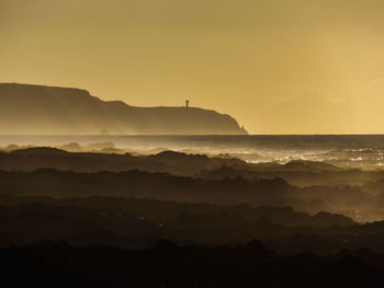 Scenic view of sea and silhouette mountains against sky during sunset