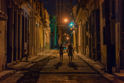 People in illuminated alley amidst buildings at night