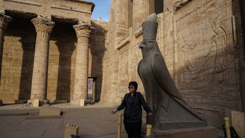 Asian tourist at edfu temple and horus granite stone statues at gate