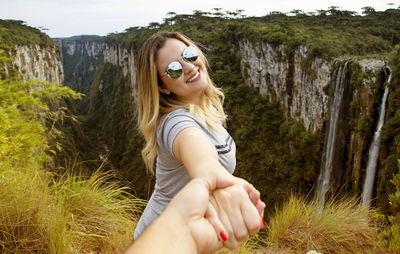 Portrait of woman holding cropped hand against cliff