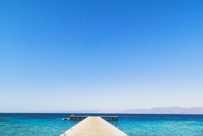 Pier over sea against clear blue sky