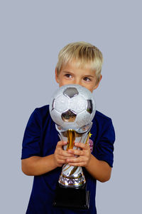 Young soccer player in blue jersey holds winners cup after the goal, isolated at light background