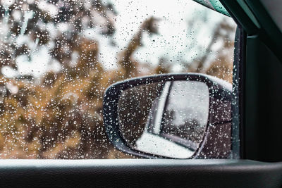 Side-view mirror seen through wet car window during rainy season