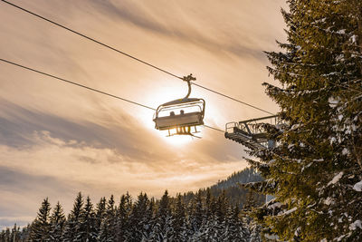 Skiers going up the ski lift, chairlift against the orange sun. snowy mountains, ski slopes, trees