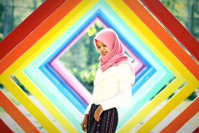 Young woman wearing hijab while standing against colorful built structure