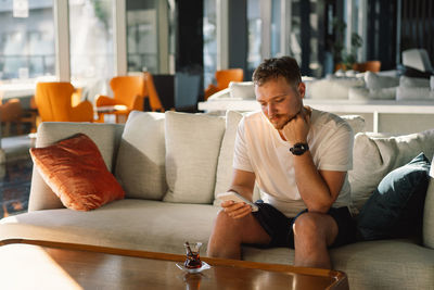 Young woman using phone while sitting on sofa at home