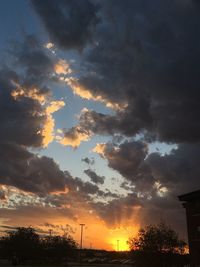 Low angle view of silhouette trees against dramatic sky during sunset