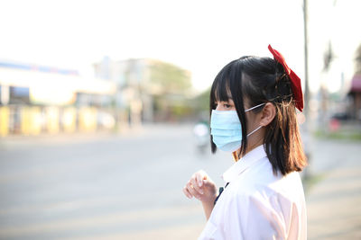 Young woman wearing mask looking away while standing outdoors