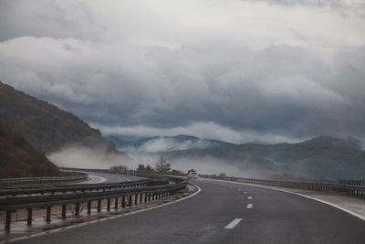 Gray smooth asphalt road in mountains turning left, opening a view of misty mountains 