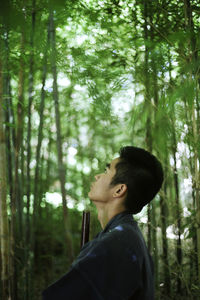 Side view of young man standing in forest