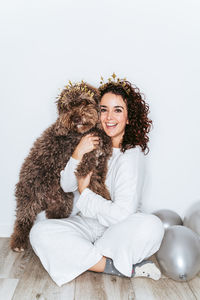 Portrait of young woman sitting with dog and balloons on floor at home