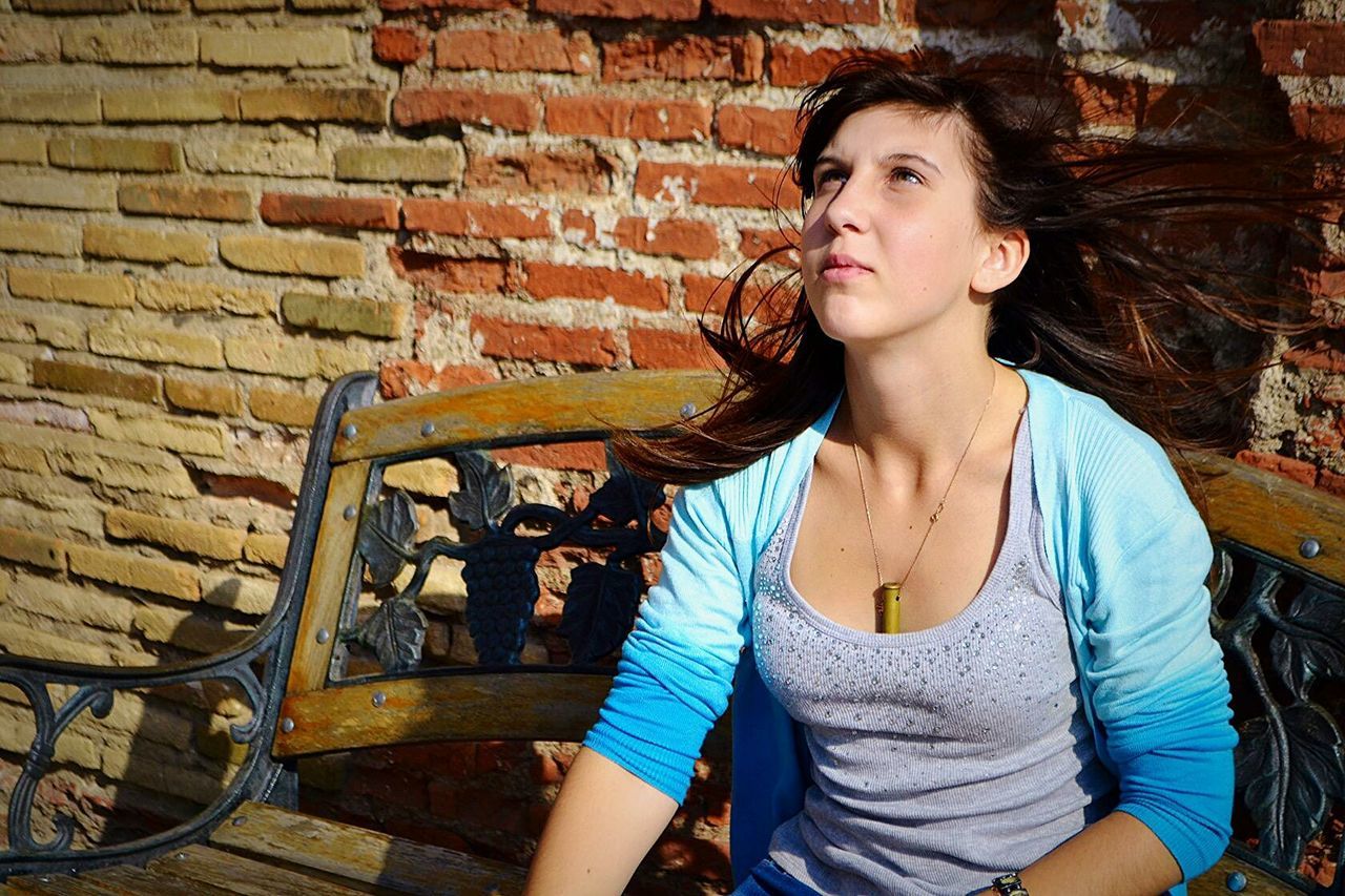 Beautiful woman sitting on bench with tousled hair against brick wall