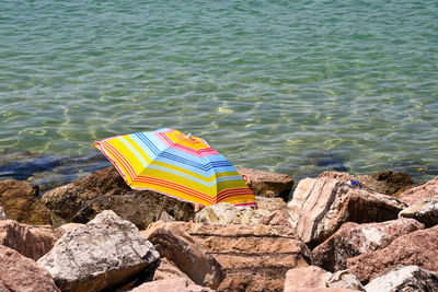 Multicolored beach umbrella on the rocky sea shore with the transparent water in the background 