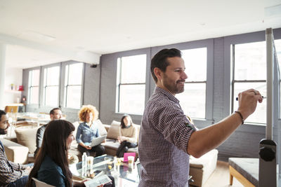 Business people looking at man writing on whiteboard in office