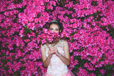 Portrait of woman holding pink flowers against plants