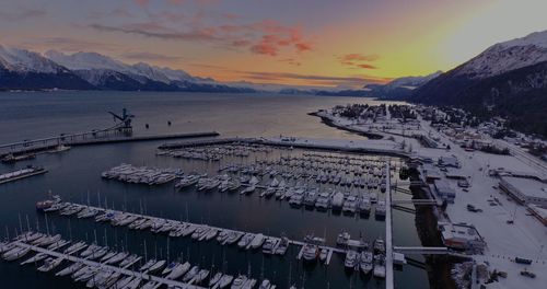 Aerial view of sea by snowcapped mountains against sky during sunset