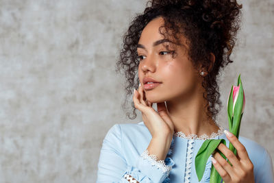 Young woman holding tulip while standing against wall