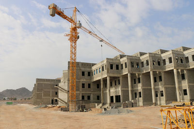 Low angle view of crane by building against sky