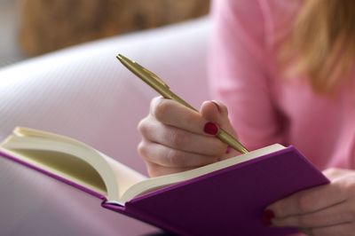 Midsection of woman writing in book at home