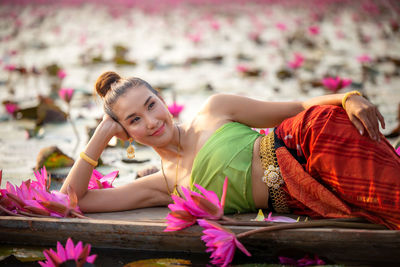 Smiling woman lying on boat by pink lotus in lake