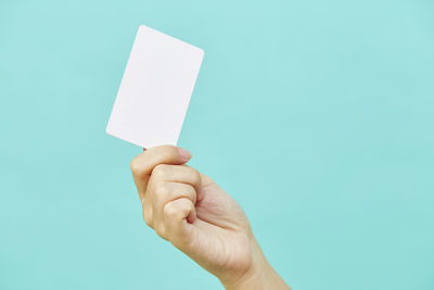 Cropped hand of person holding credit card against blue background