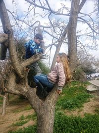 Full length of happy girl sitting on tree trunk against bare trees