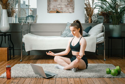 The young woman goes in for sports at home. cheerful sportswoman with blond hair meditates in lotus