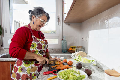 Smiling old lady cutting vegetables in the kitchen.