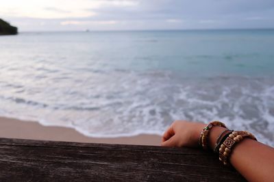 Cropped hand on pier at beach