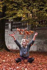 Smiling young woman playing with autumn leaves in park