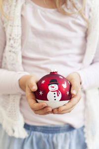 Midsection of girl holding christmas bauble at home