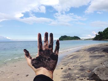 Close-up of messy hand at beach against sky