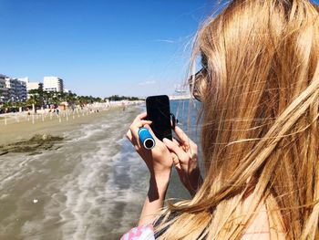Close-up of woman with blond hair using mobile phone at beach