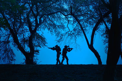 Silhouette people standing by tree on field against sky