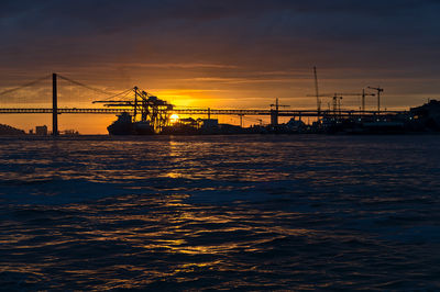 Silhouette bridge over sea against sky during sunset
