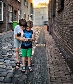 Boys using phone on street amidst buildings