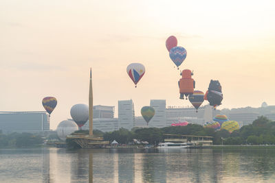 Hot air balloon flying over river against sky during sunset