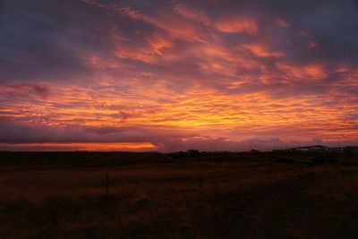 Scenic view of landscape against cloudy sky at sunset